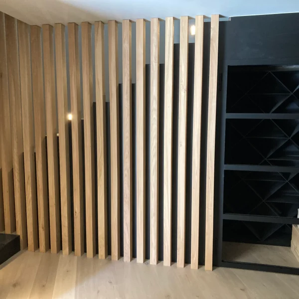Diseño interior moderno con escalera de madera y listones verticales, junto a una vinoteca negra con estantes en X.
