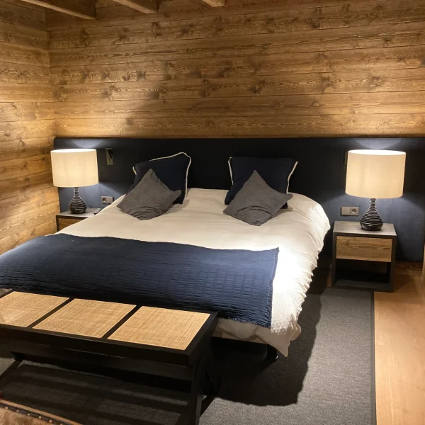 Dormitorio de estilo rústico con paredes de madera, cama doble con ropa de cama blanca y azul, y mesitas de noche con lámpara