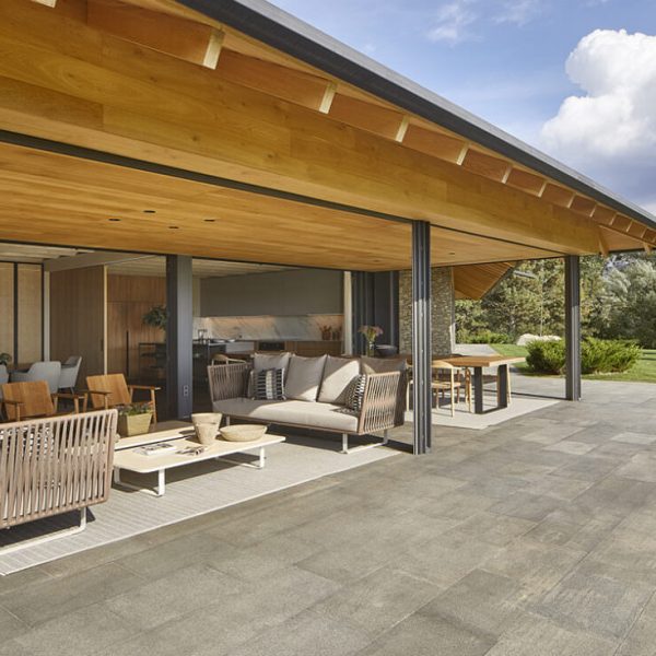 Amplia terraza exterior con mobiliario moderno y techo de madera, conectada a un interior luminoso con comedor y cocina.