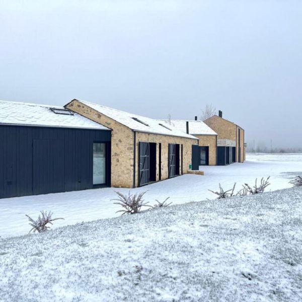 Casas modernas de piedra y madera oscura con techos nevados en un paisaje invernal, campo cubierto de nieve