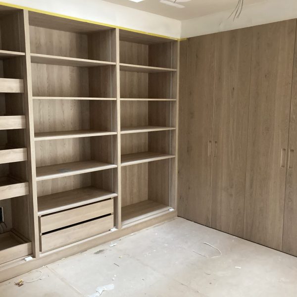 Armario y estanterías de madera a medida en proceso de instalación, mostrando la calidad artesanal de Adam Fusteria.
