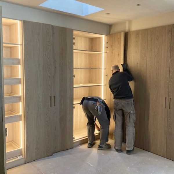 Carpinteros instalando armarios de madera a medida con iluminación LED integrada, mostrando la artesanía de Adam Fusteria.