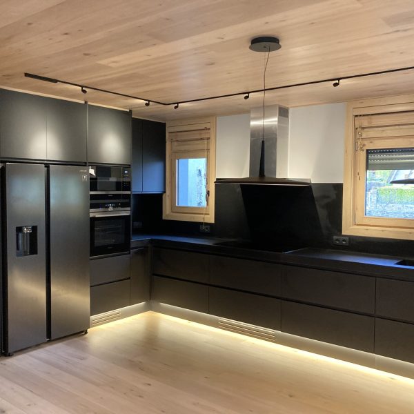 Moderna cocina con gabinetes negros, electrodomésticos de acero inoxidable, iluminación LED y techo de madera clara.