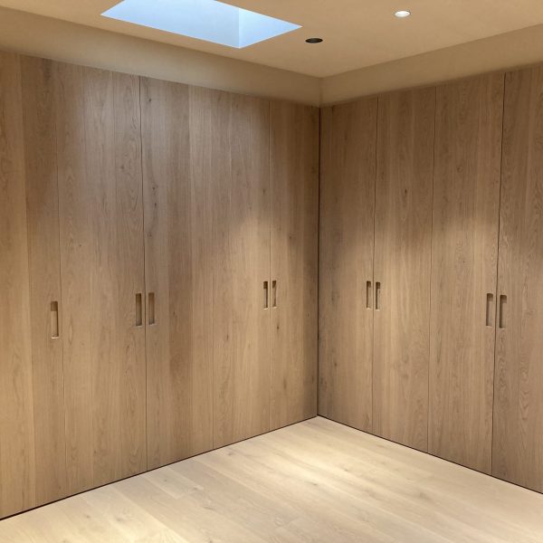Armario empotrado de madera clara con diseño moderno y minimalista, puertas sin tiradores visibles en un dormitorio.