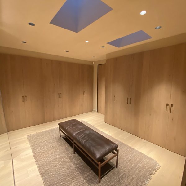 Amplio vestidor moderno con armarios de madera clara, banco de cuero marrón y tragaluces que aportan luz natural.