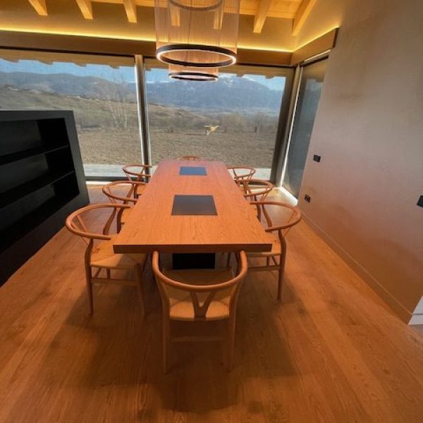 Comedor moderno con mesa de madera, sillas de diseño y vistas panorámicas a montañas y paisaje natural.