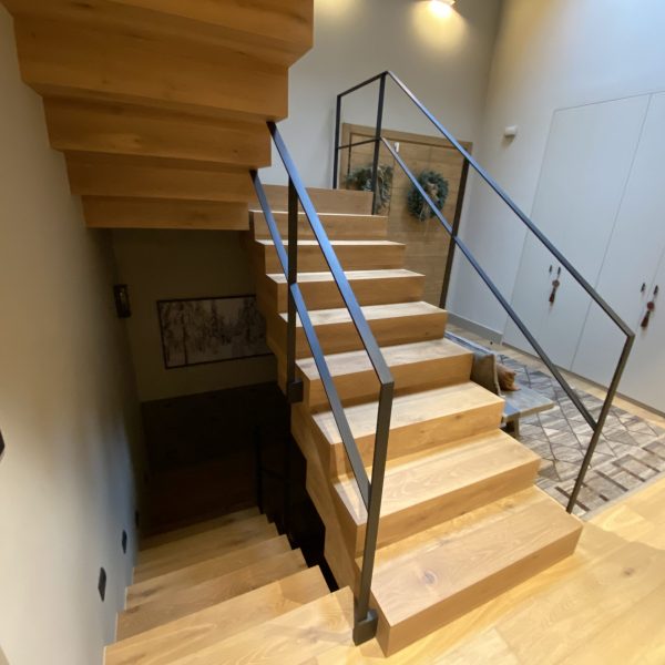 Escalera moderna de madera clara con barandilla de metal negro en un interior contemporáneo, iluminada por luz cálida.