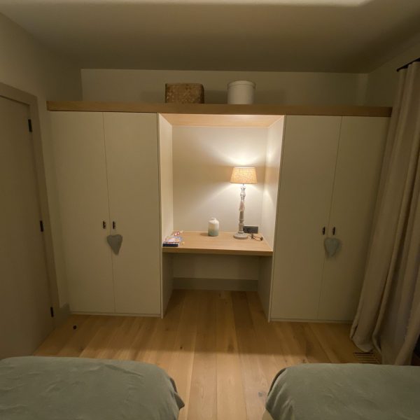 Dormitorio moderno con dos camas individuales, armario empotrado blanco, escritorio de madera y lámpara de mesa iluminada.