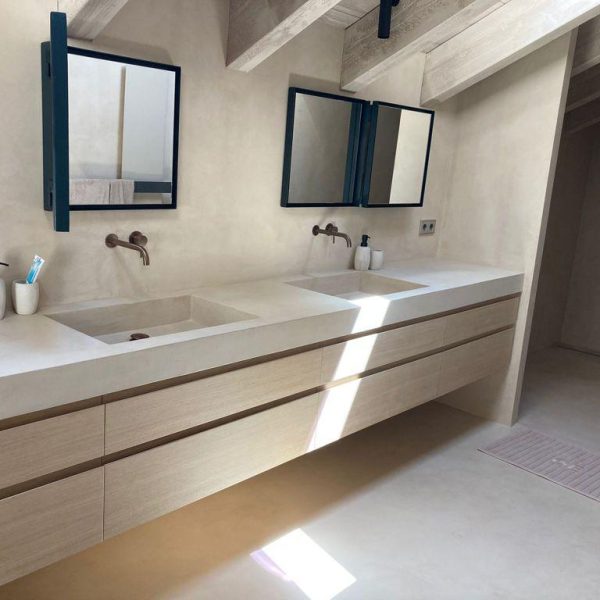 Baño moderno con doble lavabo de hormigón, grifos de bronce, espejos con marco negro y tocador de madera clara.