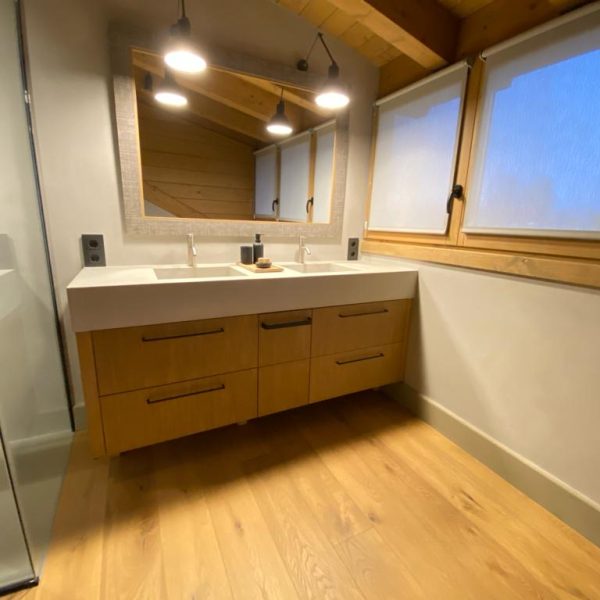 Baño moderno con doble lavabo, encimera blanca, mueble de madera clara, espejo grande y ducha de cristal.